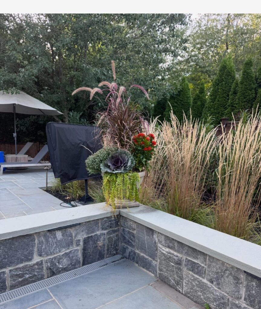 Fall planter with ornamental grass, flowering plants and ornamental kale on a stone patio